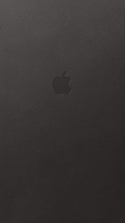 Pebbled brown-black leather fills the frame, an Apple mark pressed into it just above centre with almost no contrast against the hide.