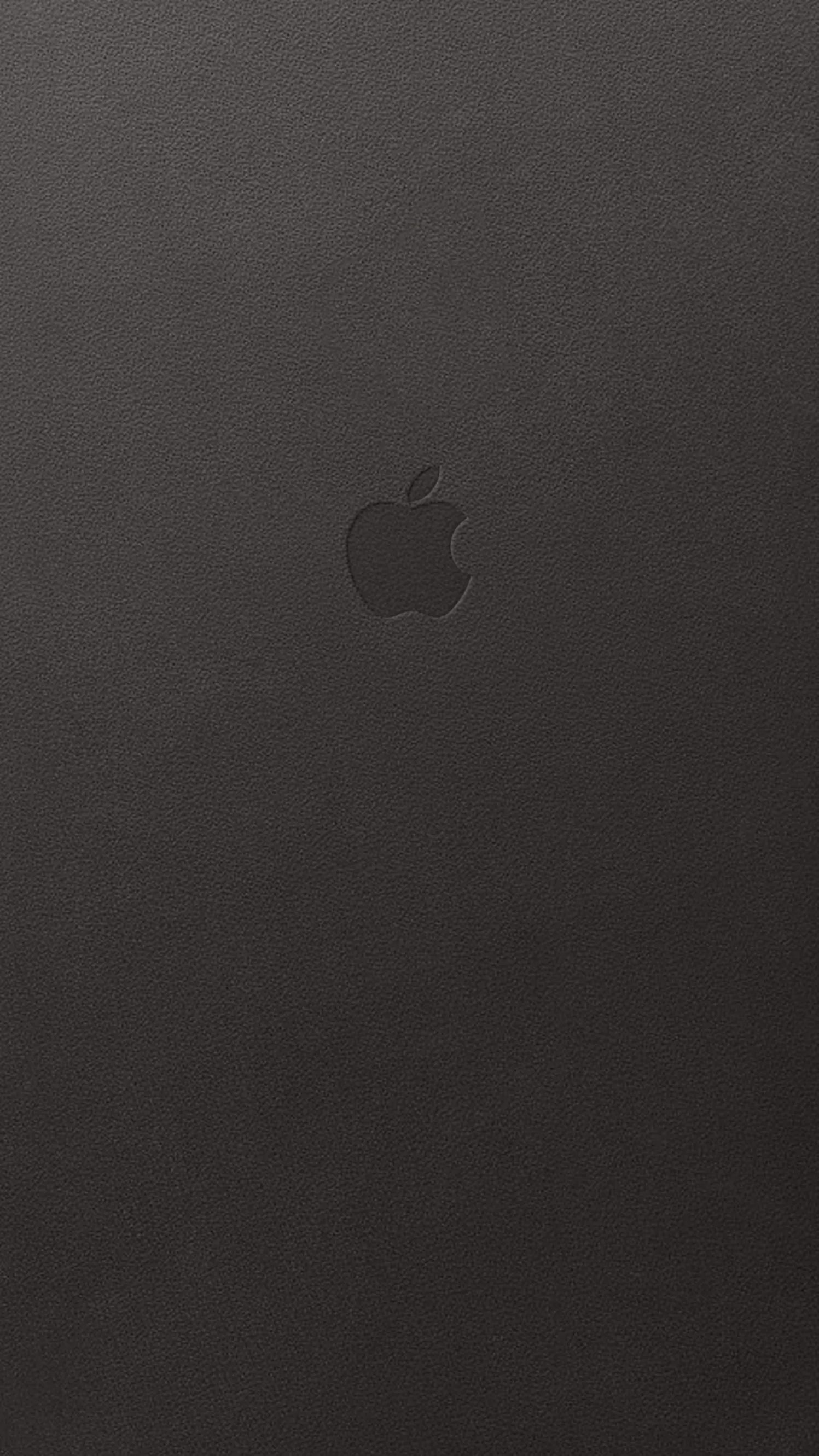 Pebbled brown-black leather fills the frame, an Apple mark pressed into it just above centre with almost no contrast against the hide.