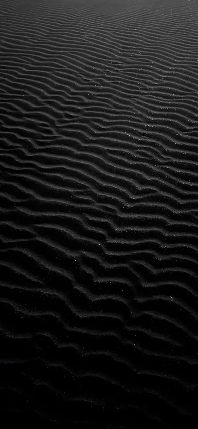 Parallel wind ripples run across dark volcanic sand toward a horizon that dissolves into black, lit from a low raking angle.
