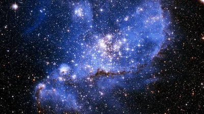 A dense cluster of newborn stars burns white at the heart of this blue nebula, surrounded by dark dust ridges and a sky packed with stars.