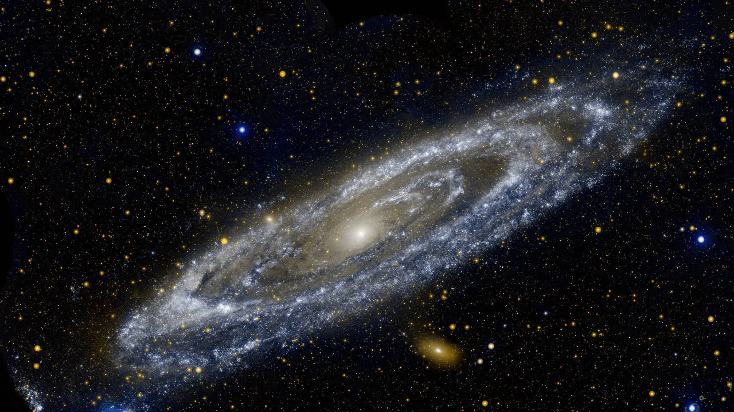 The Andromeda galaxy tilts across a field of foreground stars, a yellow core wrapped in blue arms with a small companion galaxy below.