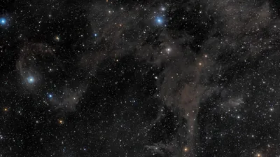 Thin brown and grey dust lanes drift over a crowded field of blue and orange stars, the sort of view a long-exposure astrophoto gives.