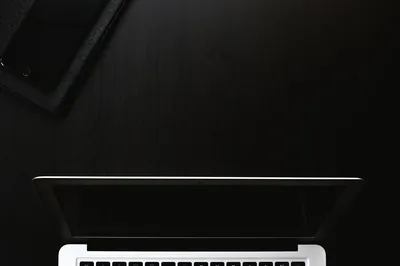 An open laptop sits at the bottom of the frame with a phone in the top corner, the desk between them left empty.