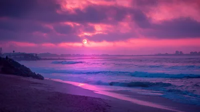 Pink haze softens a distant shoreline of buildings while teal waves roll onto dark sand, the muted tones easy behind white lock-screen text.