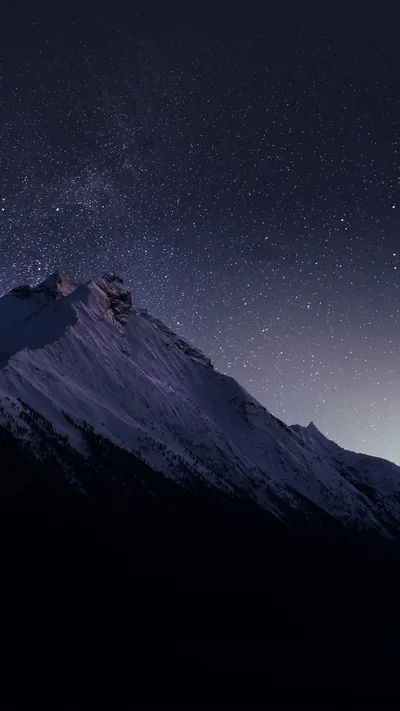 A snowy ridgeline sits below a sky dusted with stars, the dark navy upper two-thirds keeping the lock-screen clock legible.