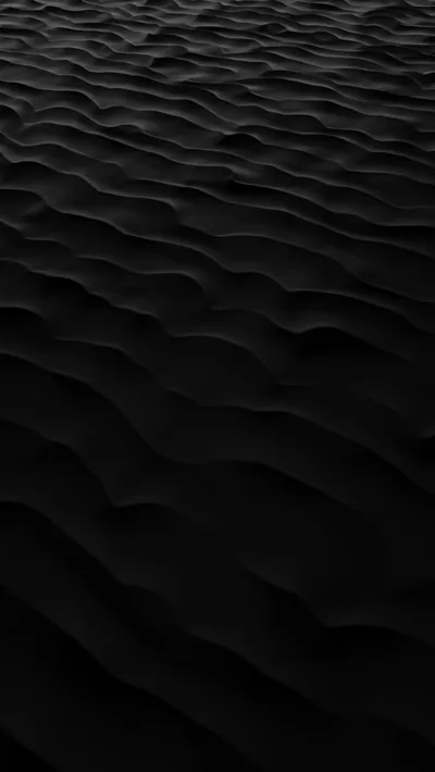 Wind ripples run in rows across dark sand shot from a low angle, the ridges catching light while the troughs stay unlit.