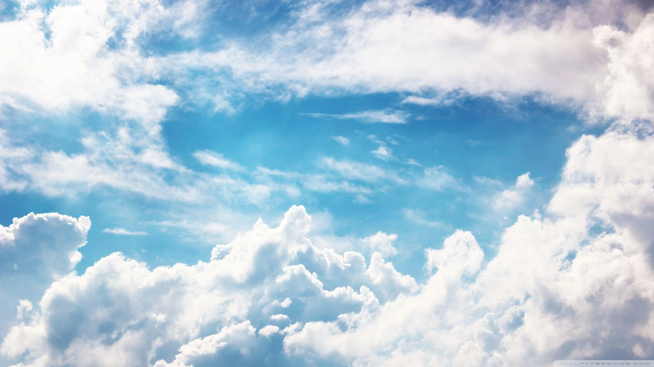 Bright cumulus crowds in from every edge, leaving an open pool of blue at centre frame where desktop icons sit clearly.