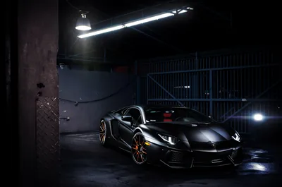 A single fluorescent tube hangs over the matte black wedge of the car, a second light flaring in from the right across bronze wheels.