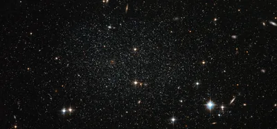Thousands of faint stars fill the frame with a few small elliptical galaxies among them, the whole scene kept dim and low-contrast.