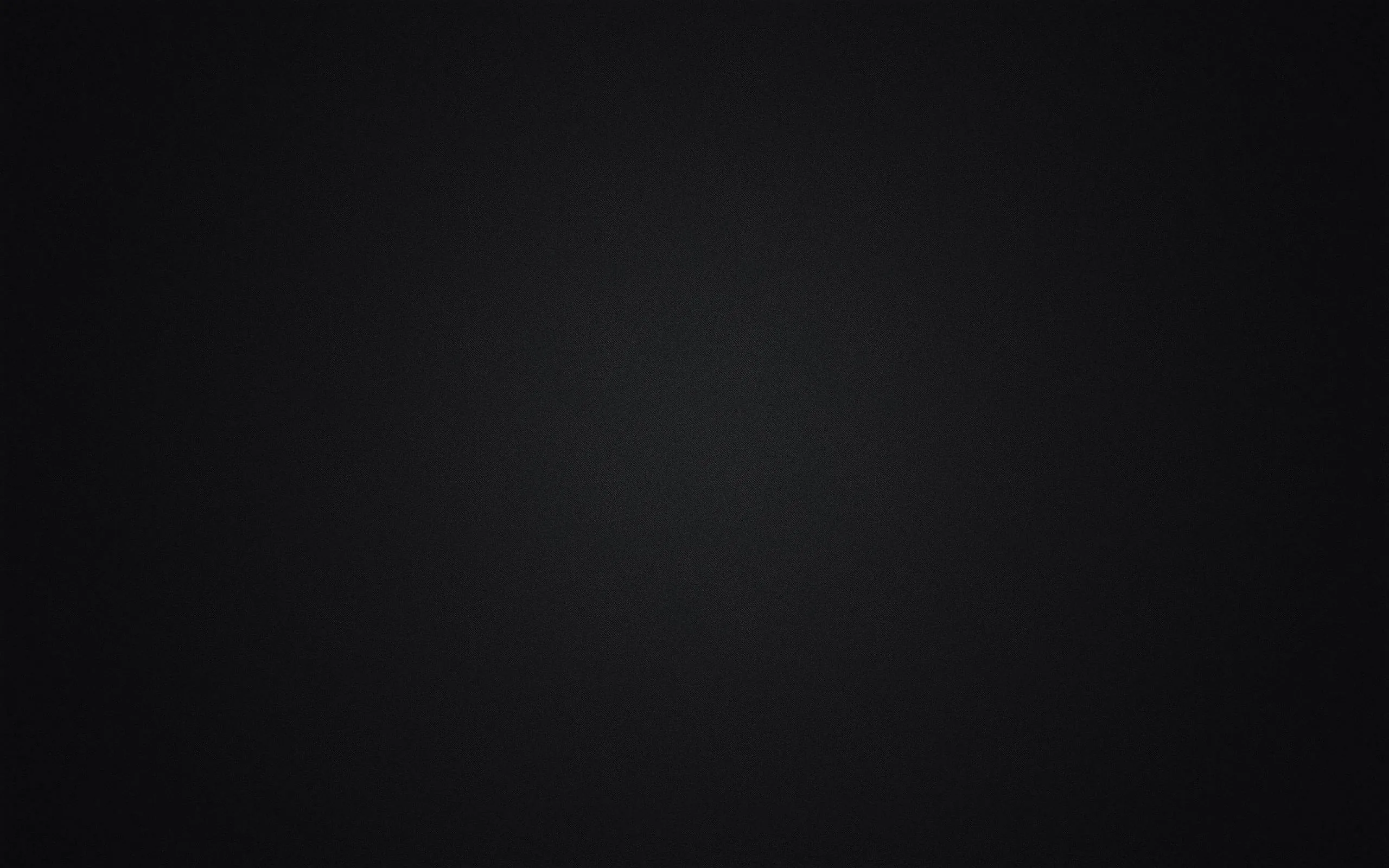 An empty studio wall lit from the middle, a wide grey pool of light fading evenly outward until the corners go fully black.