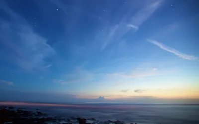 First stars prick through a blue twilight over a long-exposure sea, the last orange of sunset held low on the right horizon.
