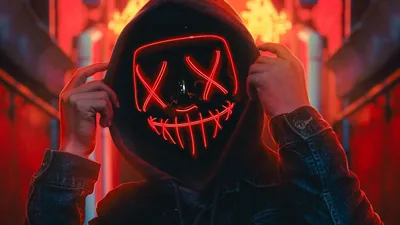 A figure grips the sides of a red wire-light mask with X eyes, a red-lit corridor blurring behind, the jacket falling into shadow at the bottom edge.