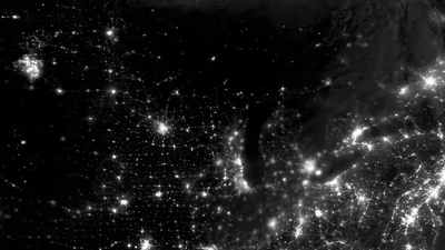 Night-side city lights spread across a continent in monochrome, coastlines and lake edges drawn only by where the lights stop.