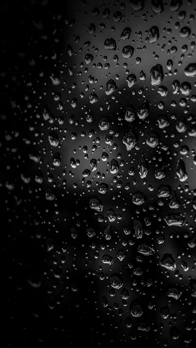 Water beads cling to a pane of glass shot in near darkness, the left edge falling away to black while a soft grey light picks out each drop.