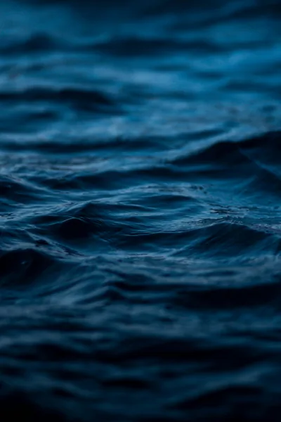 Small night swells roll through a narrow band of focus mid-frame, the bottom third blurring into near-black water where docked app icons stay legible.