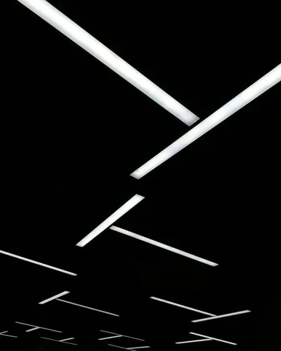 Long white light bars cross at angles overhead and repeat smaller into the distance, everything between them left black.