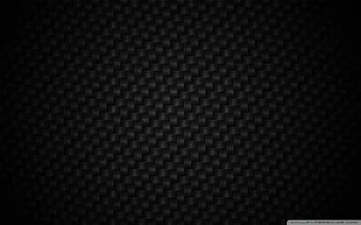 The tight over-under weave of carbon fibre fills the frame, lit from the upper left so the sheen falls off into black at the corners.