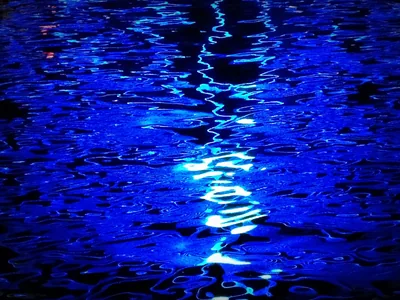 A single white light reflects as a broken vertical streak down rippled water at night, both side edges sinking into true black for OLED.