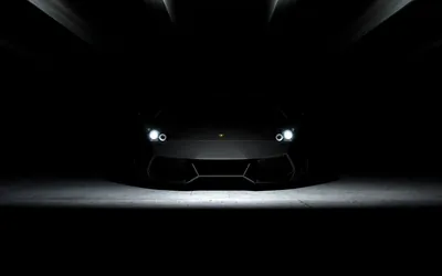 Only the headlights and a thin strip of lit floor reveal a low sports car, the roof and everything behind it swallowed by the dark.