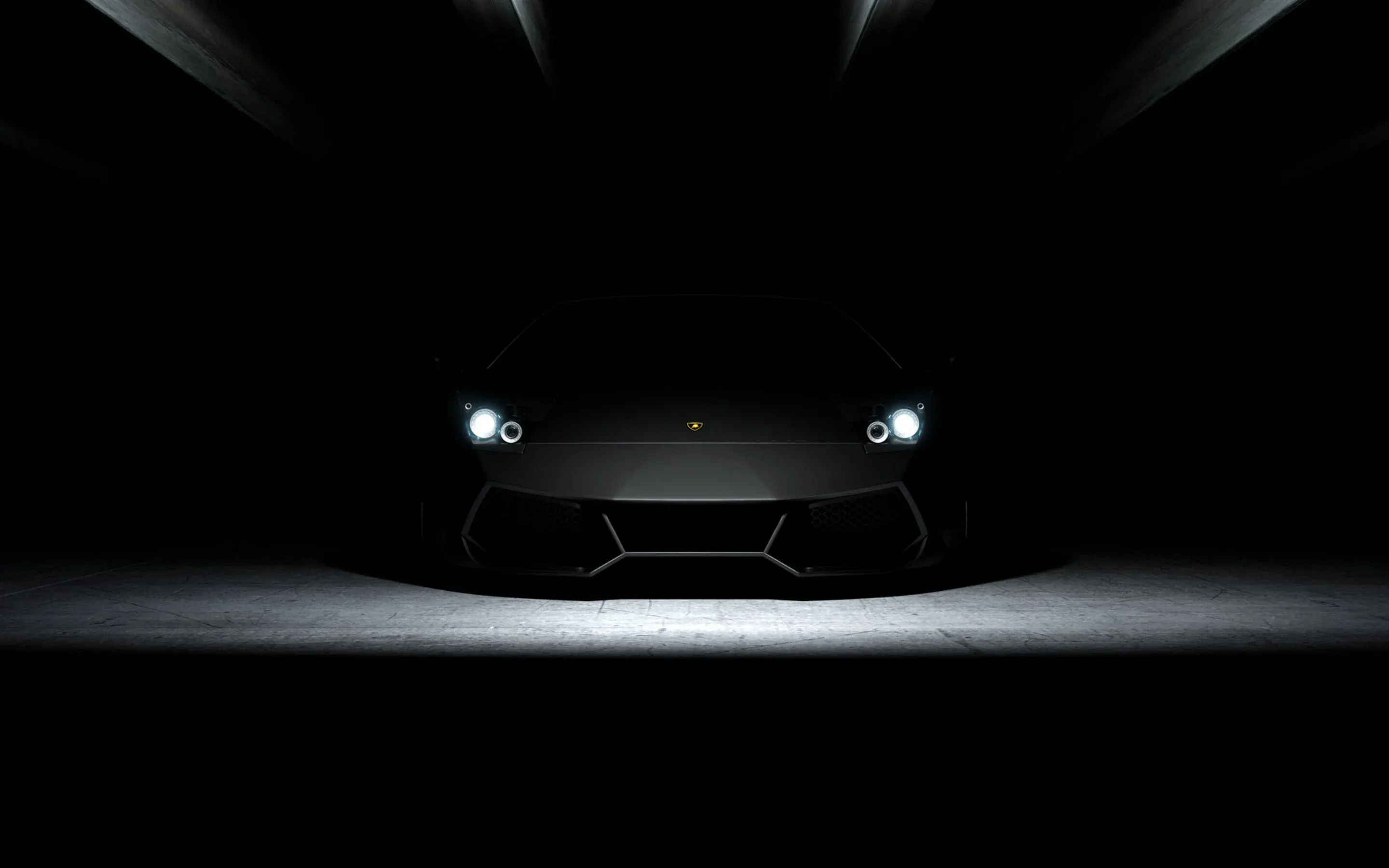 Only the headlights and a thin strip of lit floor reveal a low sports car, the roof and everything behind it swallowed by the dark.