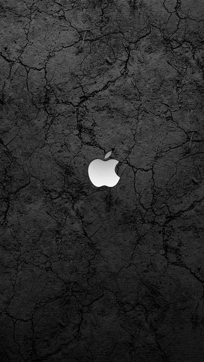 Dry cracked ground fills the frame in grey and black, with the Apple logo glowing white just above centre like a light behind the surface.