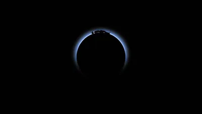A thin arc of blue light rims a dark sphere with a tiny figure seated at its crown; beyond that ring the frame is total black, easy on OLED batteries.