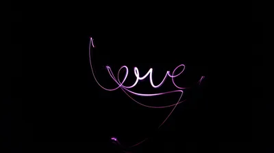 The word love traced in thin purple light against total darkness, a long-exposure trail looping back under the letters.