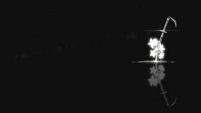 A single spray of white light flares on the right side of a black field, its reflection breaking apart on the water below.