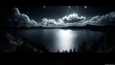 Moonlight breaks through heavy cloud and lays a bright path down the middle of a still lake, pines in silhouette along the near shore.
