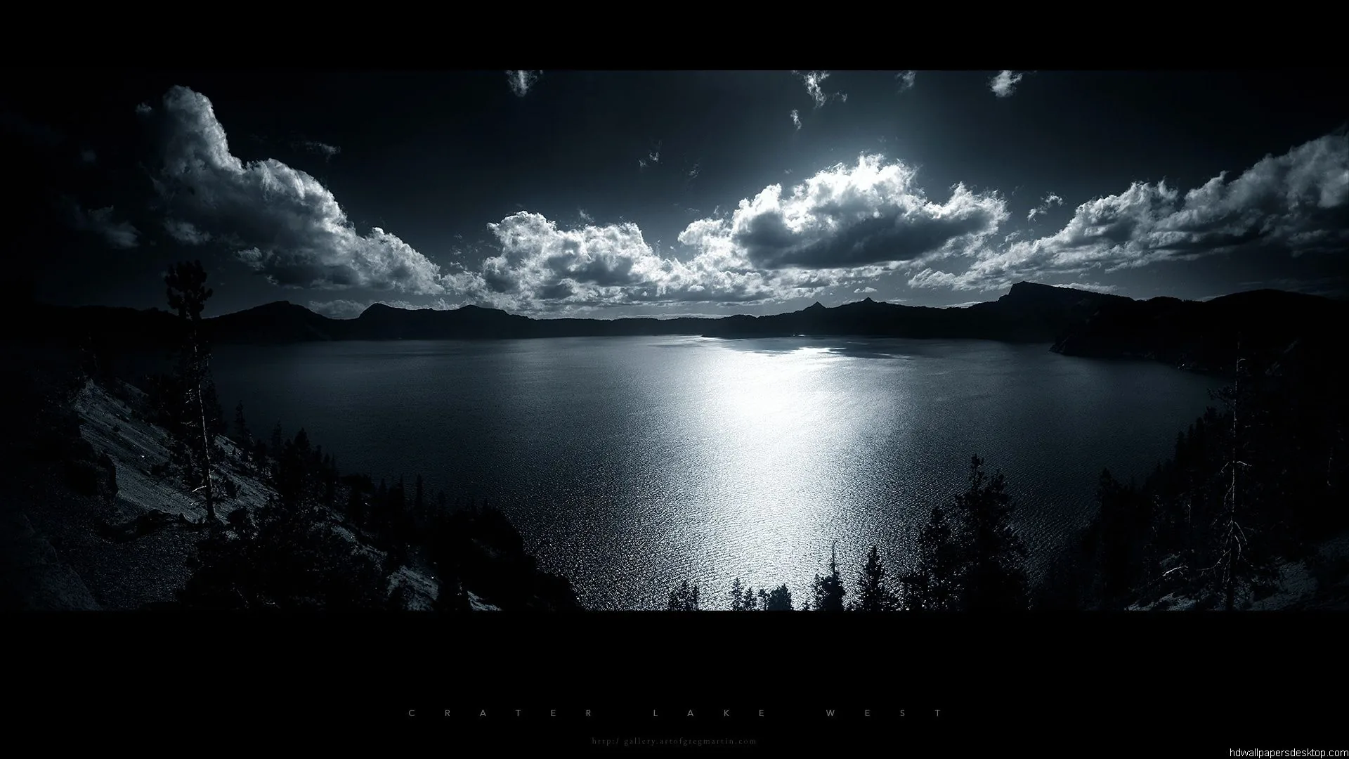 Moonlight breaks through heavy cloud and lays a bright path down the middle of a still lake, pines in silhouette along the near shore.