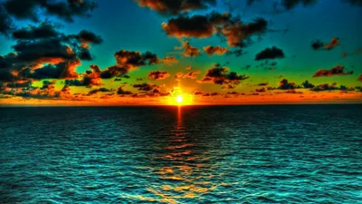 The sky grades from green to orange around a sinking sun, its gold reflection cutting a line through dark rippled sea toward the viewer.