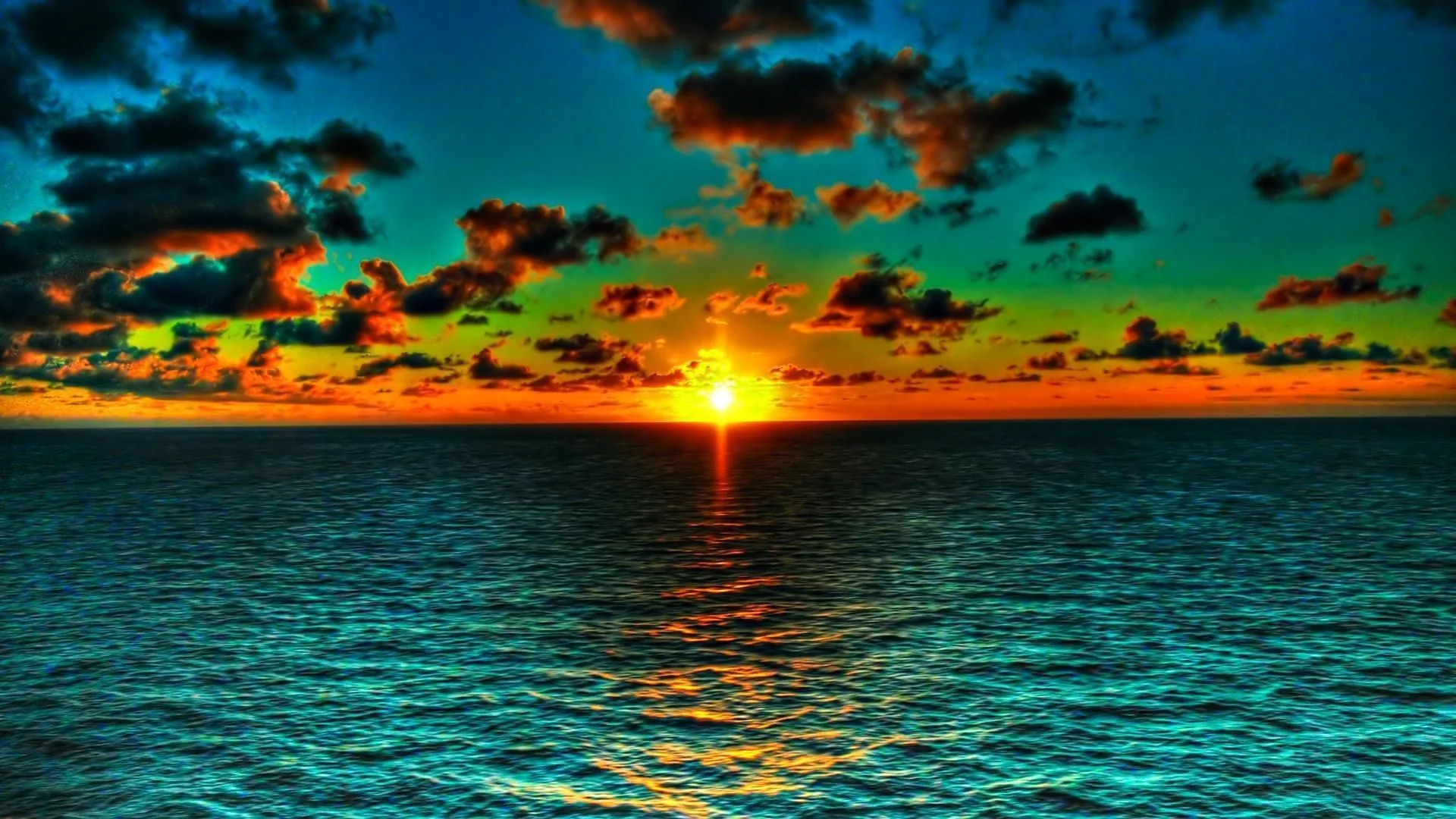 The sky grades from green to orange around a sinking sun, its gold reflection cutting a line through dark rippled sea toward the viewer.