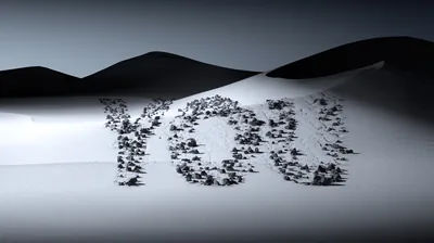 Small dark stones spell a short word across a pale dune field, the ridges rolling away behind it.