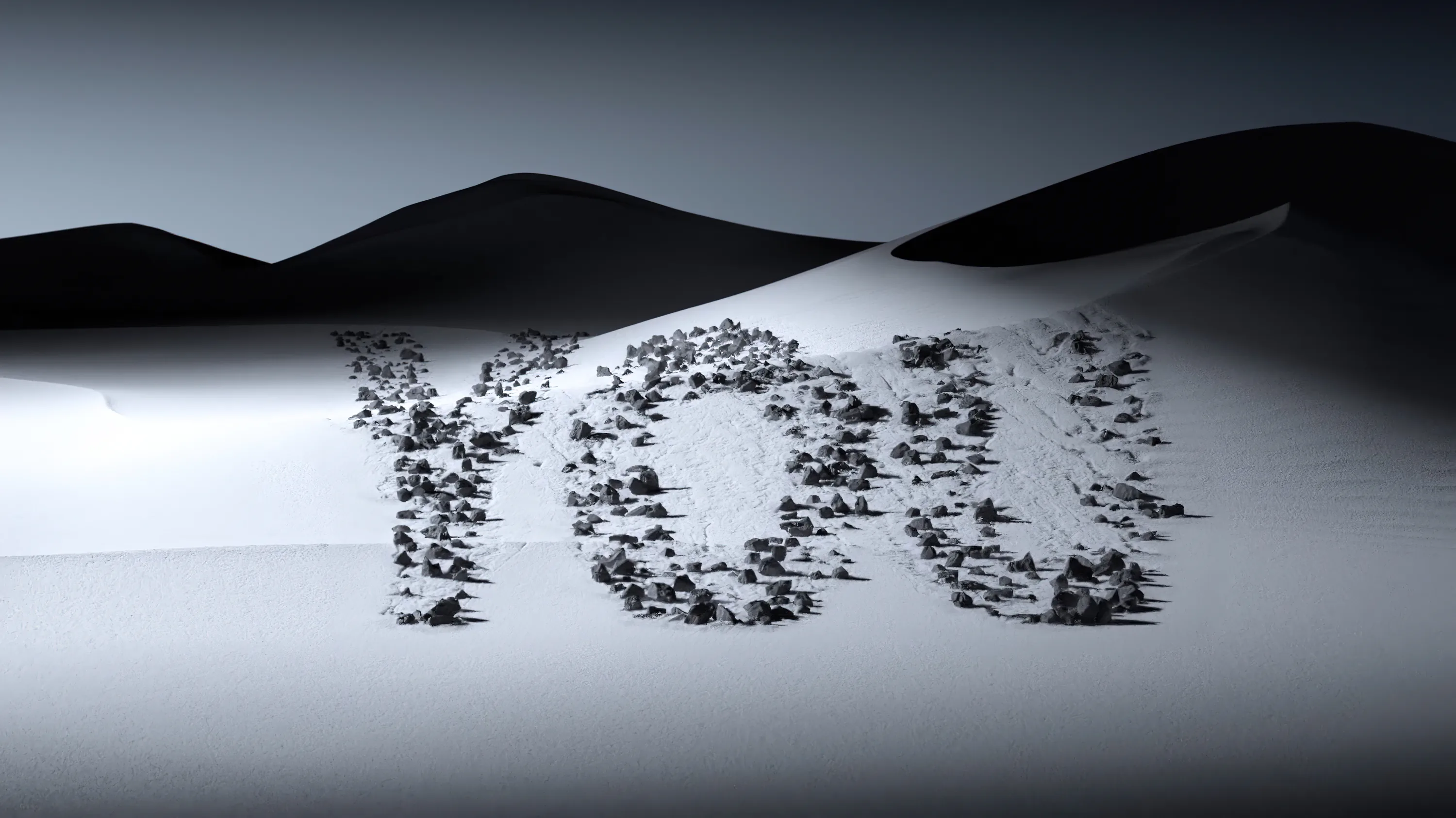 Small dark stones spell a short word across a pale dune field, the ridges rolling away behind it.
