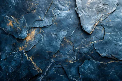 Layered slate stone in matte steel blue, its flaked edges catching pale light, with amber mineral streaks burning through the lower left and centre.