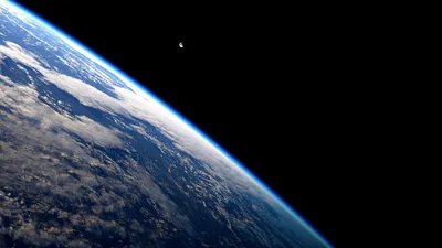 Thick cloud bands sweep the sunlit limb from the lower left, while the right half of the frame stays empty black space under a lone Moon dot.