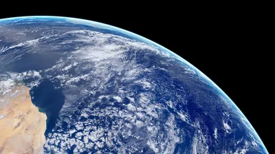 The desert shore anchors the lower left while cloud-flecked ocean stretches to the planet's curve, the upper right corner left as black space.