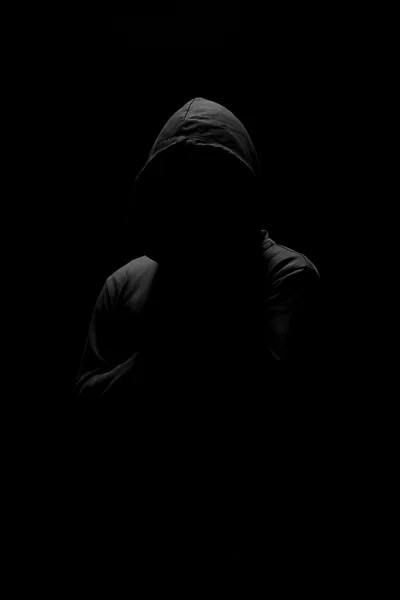 A hooded silhouette stands against black, the face completely lost to shadow.