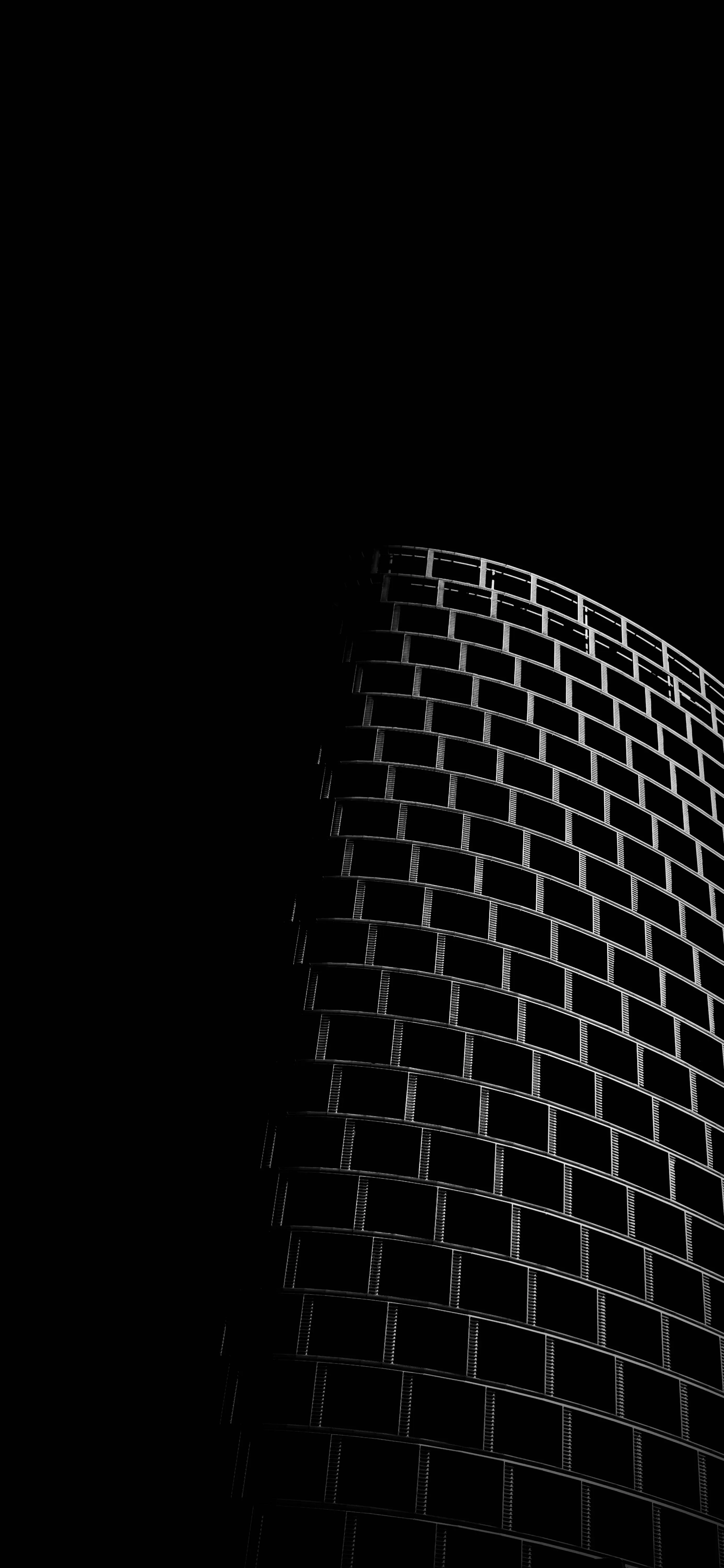 The curved brick face of a tall building catches a thin sidelight along its edge while the left half of the frame stays completely black.