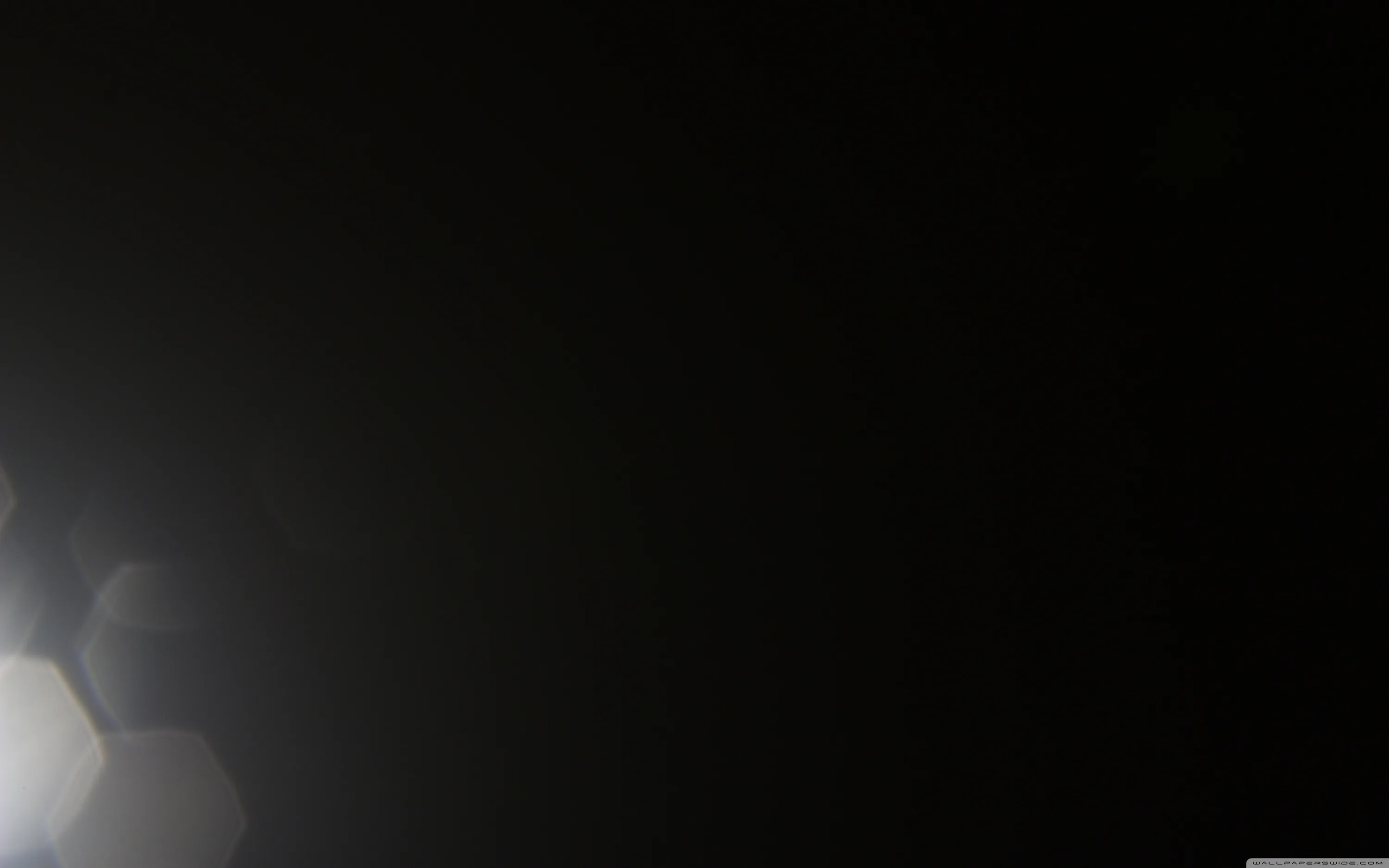 Near-total black broken by a chain of pale hexagons drifting in from the lower left, the kind of flare a bright light leaves off frame.