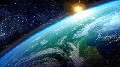 Seen from orbit, teal-green ocean and cloud swirls roll toward a sun flare at the top edge, star-dusted black filling both upper corners.