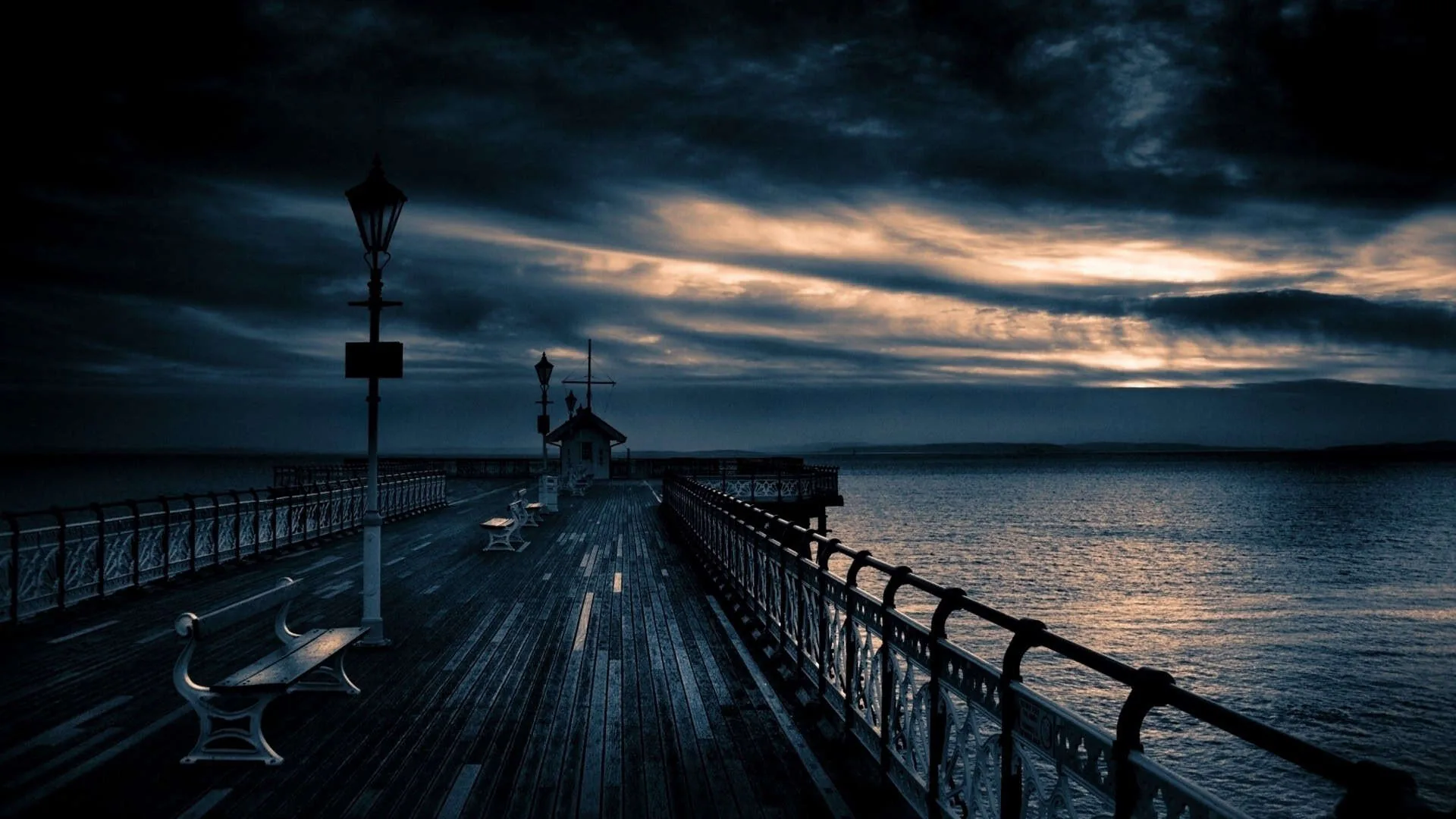 Wet planks and iron railings run straight out to a small pavilion, a bench and a lamp post on the left, storm cloud breaking over the water on the right.