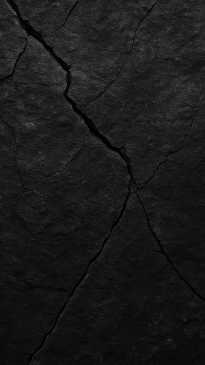 Deep cracks fork down a slab of black stone, side light raking the surface to bring out every pit and grain.