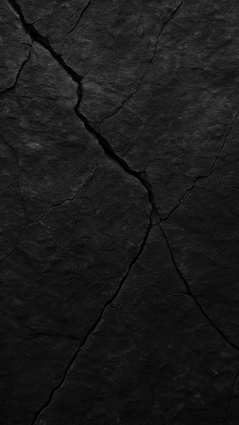 Deep cracks fork down a slab of black stone, side light raking the surface to bring out every pit and grain.