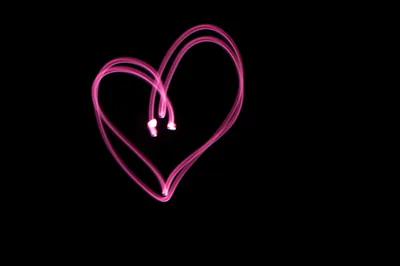 A single loop of magenta light traces a heart in a long-exposure shot, the two ends of the stroke crossing near the centre and the rest of the frame pure black.