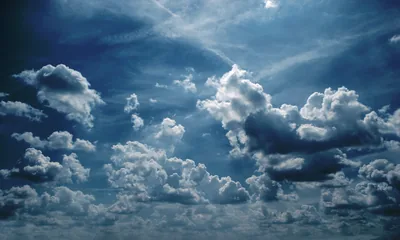 Small moody cumulus scatter across a steel-blue sky, two faint contrails crossing near the top — the whole frame reads almost monochrome.