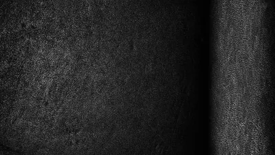 A gritty near-black wall runs edge to edge, a soft vertical band of light grazing the right side and the rest sinking into shadow.