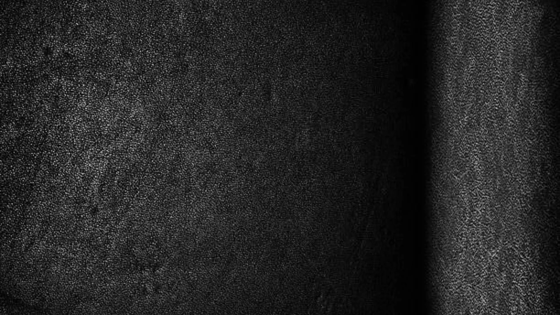A gritty near-black wall runs edge to edge, a soft vertical band of light grazing the right side and the rest sinking into shadow.