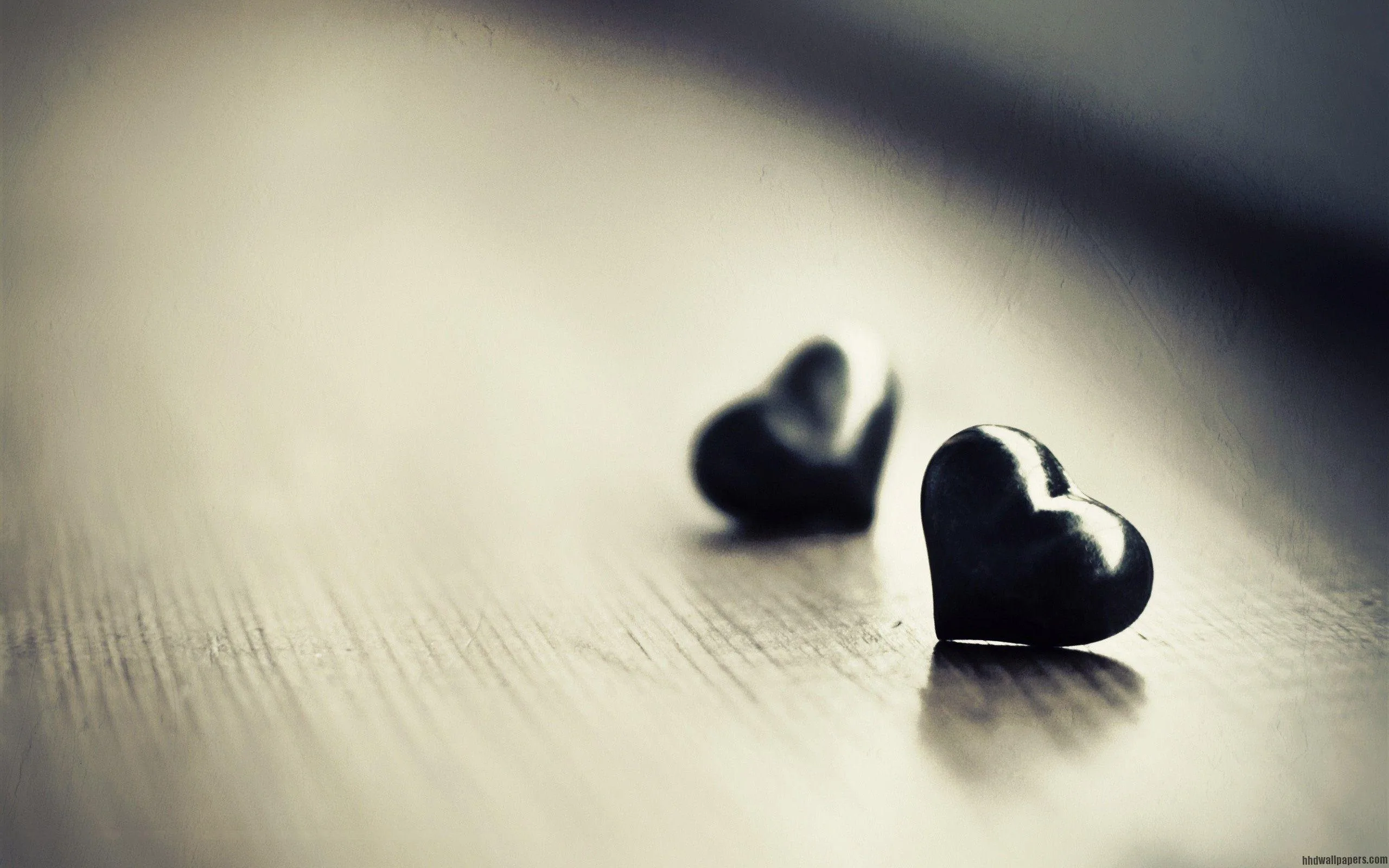 A pair of small dark hearts on bare wood in washed-out grey, the nearer one sharp and the other softened by shallow focus.