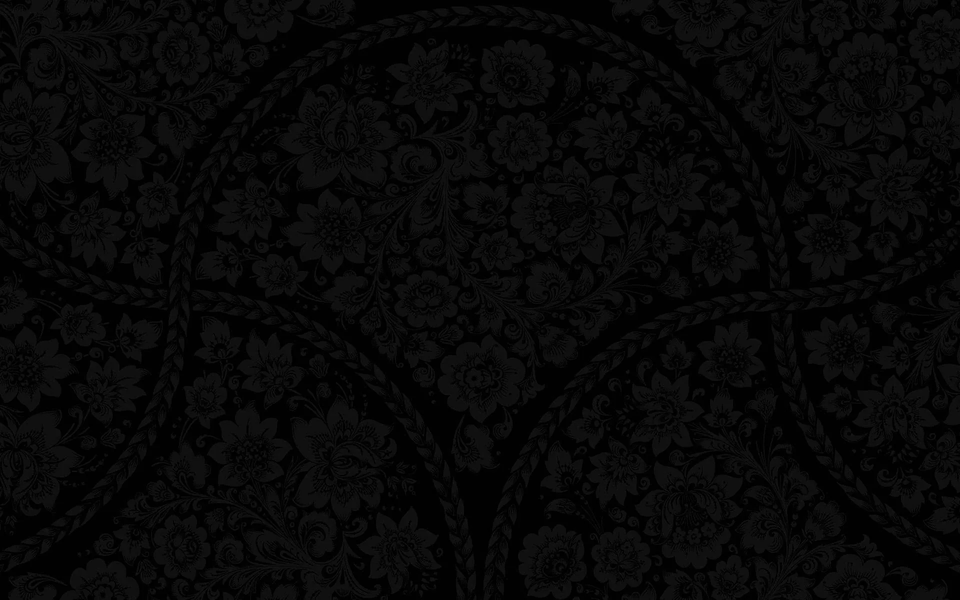 A dense floral scroll pattern is pressed into a near-black surface, the curved borders showing only where the light grazes them.